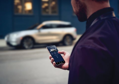 A person is shown interacting with a smartphone to connect to a Lincoln vehicle across the street. | Bill Knight Lincoln in Tulsa OK