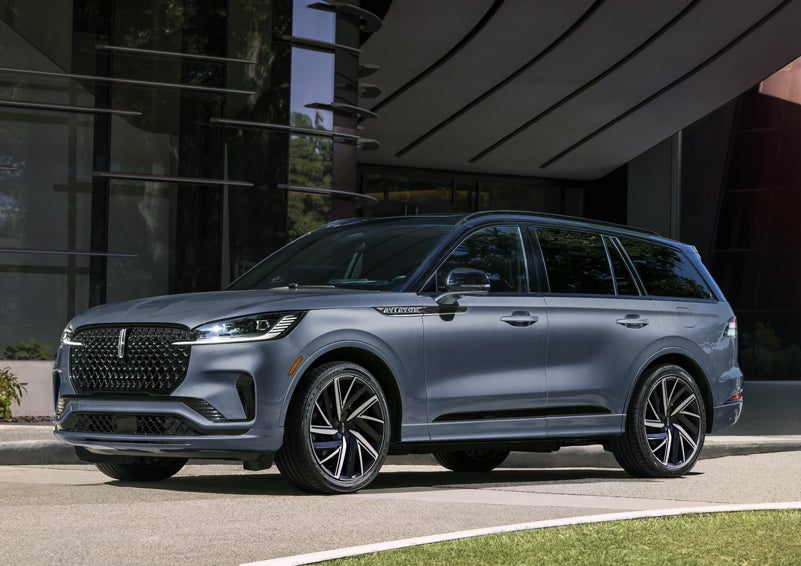 A gray 2025 Lincoln Aviator® SUV is parked outside a modern building showcasing the driver’s side of the vehicle. | Bill Knight Lincoln in Tulsa OK