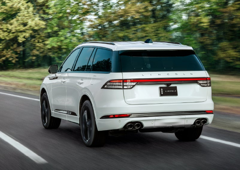 A white 2026 Lincoln Aviator® SUV is being driven away down a road lined with colorful trees. | Bill Knight Lincoln in Tulsa OK