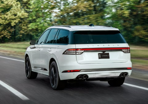 A white 2026 Lincoln Aviator® SUV is being driven away down a road lined with colorful trees. | Bill Knight Lincoln in Tulsa OK