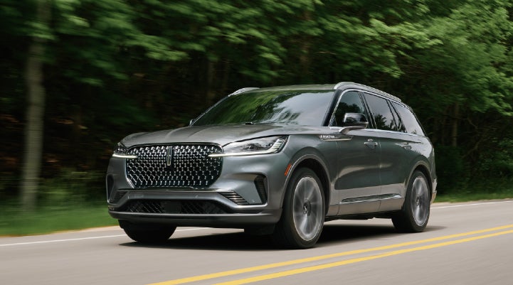 A 2027 Lincoln Aviator® SUV is being driven down a road lined with trees. | Bill Knight Lincoln in Tulsa OK